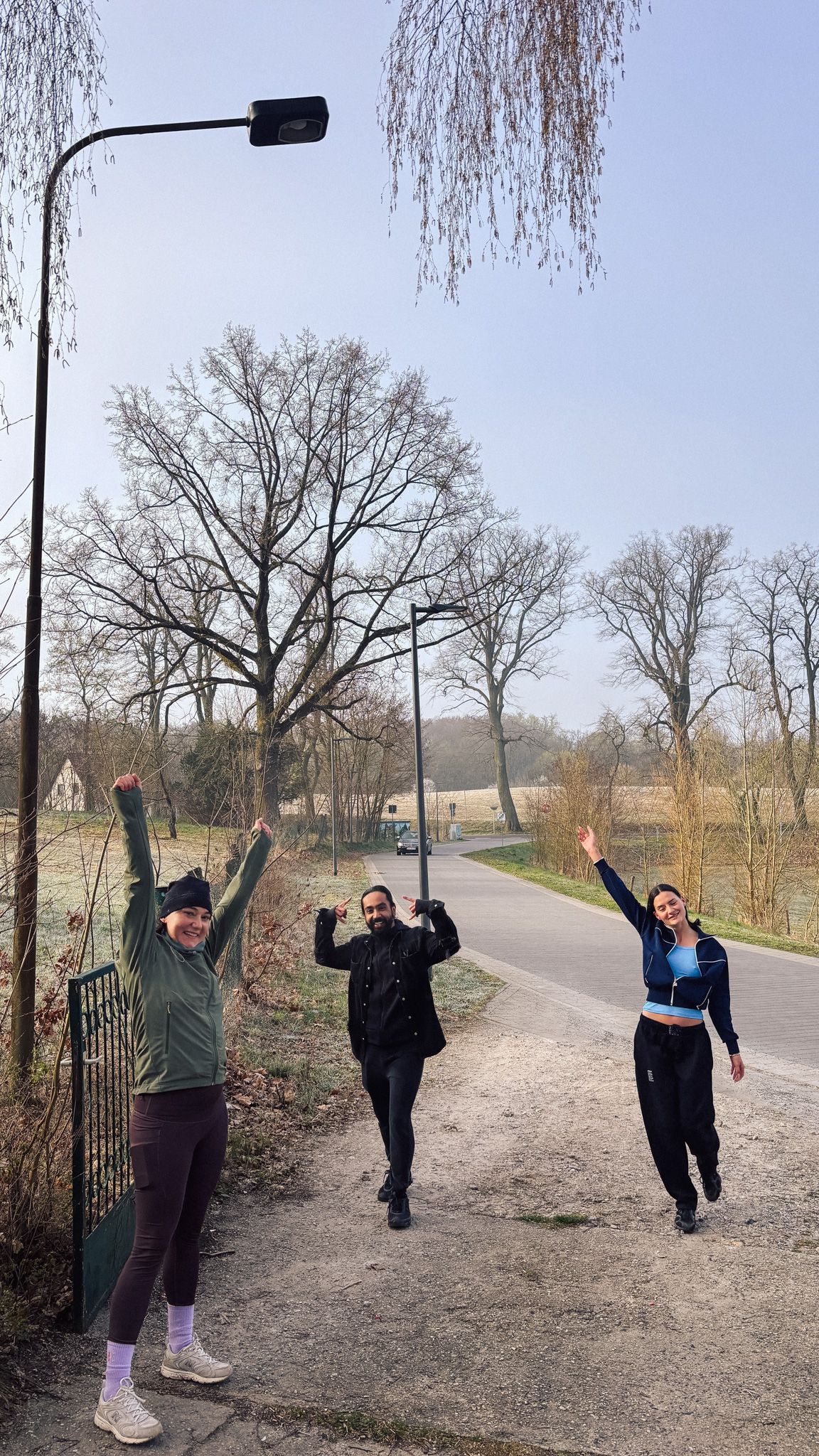Drei Personen stehen nach einer Joggingrunde im Winter freudig mit erhobenen Armen am Eingang des Grundstücks