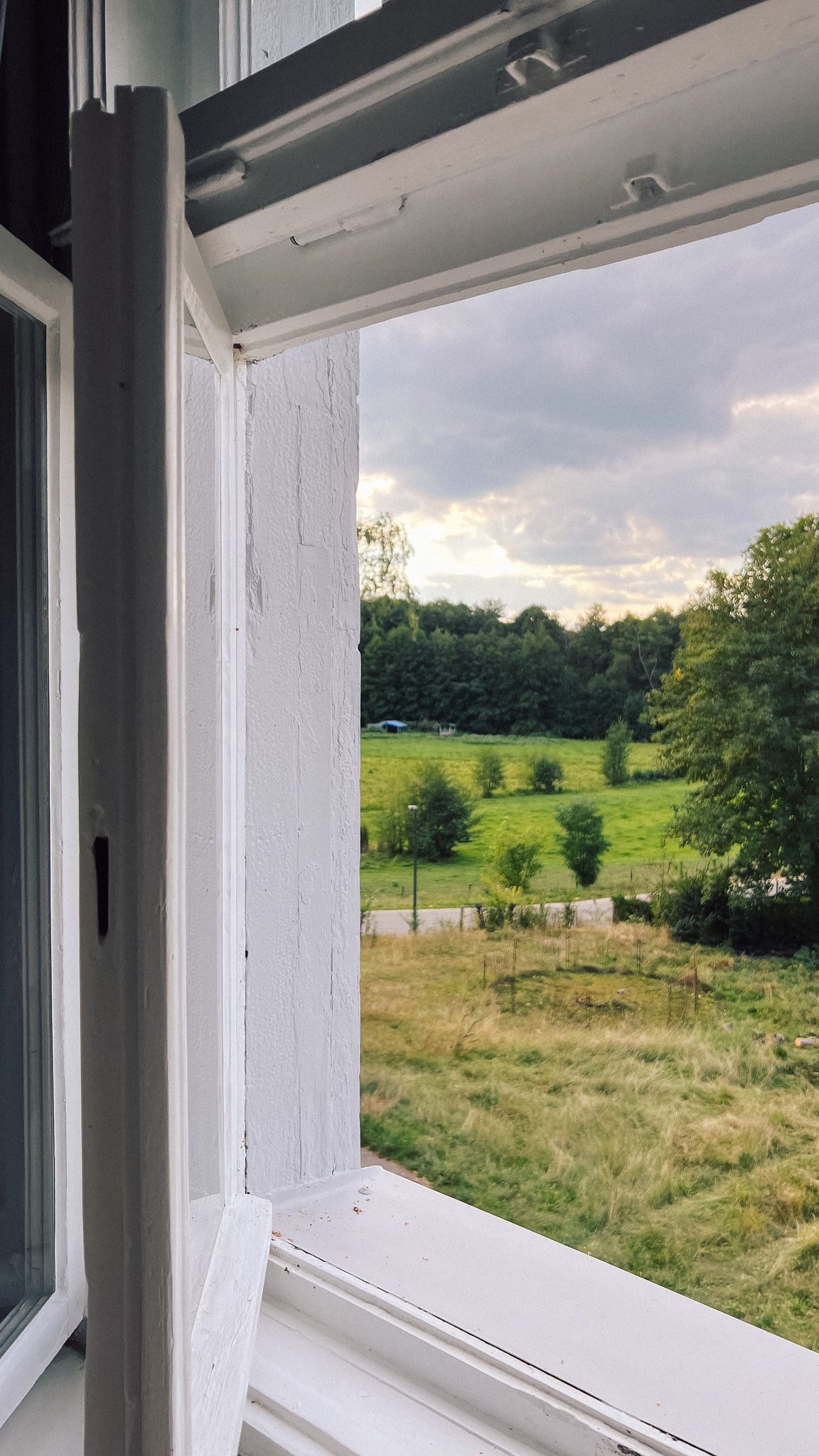 Blick aus einem Altbaufenster der Villa über Wiese und Bäume bei einer Workation in Neupitz