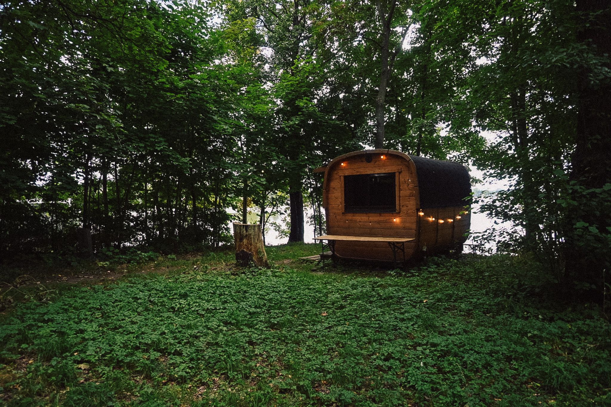 Die Holzsauna von Neupitz am Waldrand direkt am Wasser, mit beleuchtetem Fenster