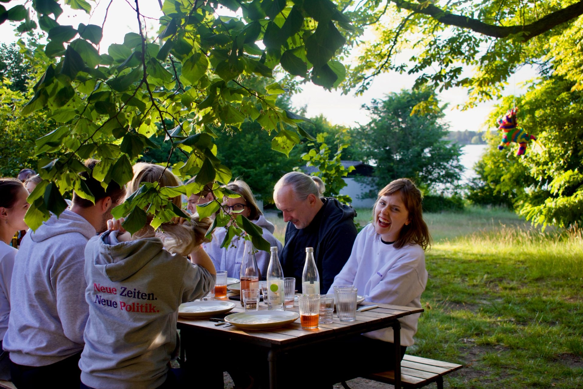Gruppe isst gemeinsam im Garten unter Bäumen in Neupitz. Frau schaut lachend in die Kamera.