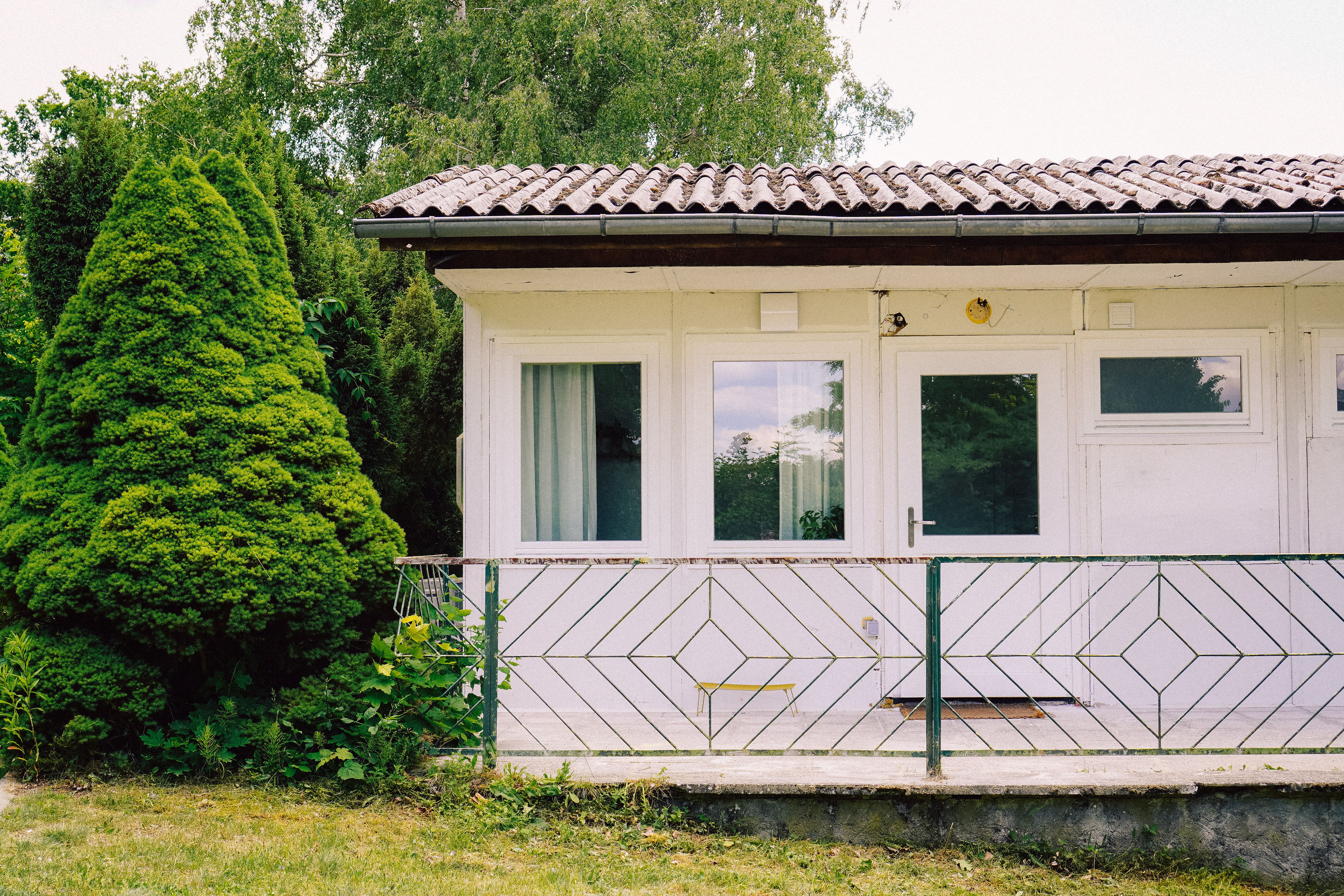 Außenansicht eines der fünf weißen Bungalows mit Terrasse, der neben Bäumen auf dem Neupitz-Gelände steht