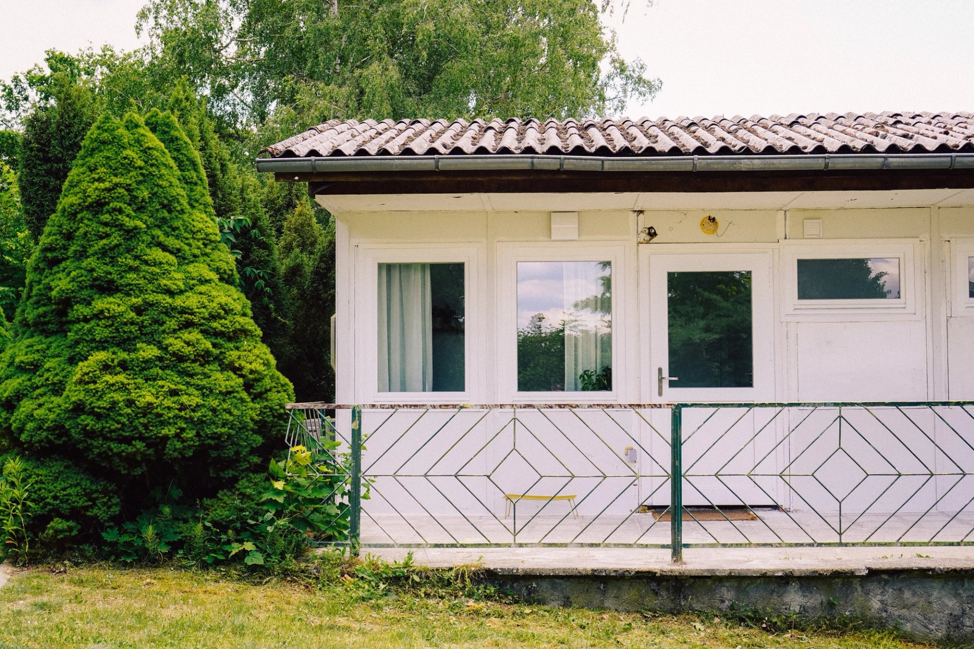 Außenansicht eines der fünf weißen Bungalows mit Terrasse, der neben Bäumen auf dem Neupitz-Gelände steht