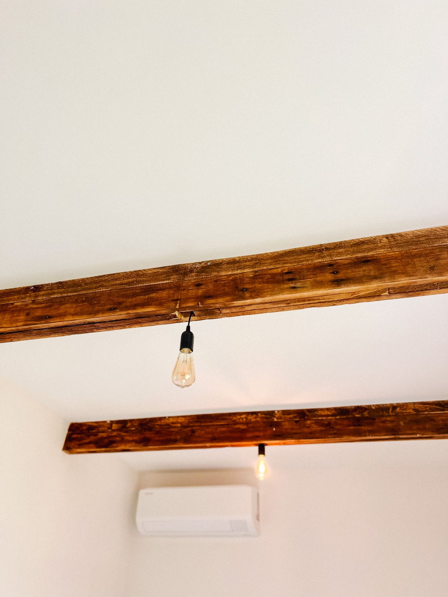 Weiße Zimmerdecke mit dunklen Holzbalken und schlichter Glühbirne