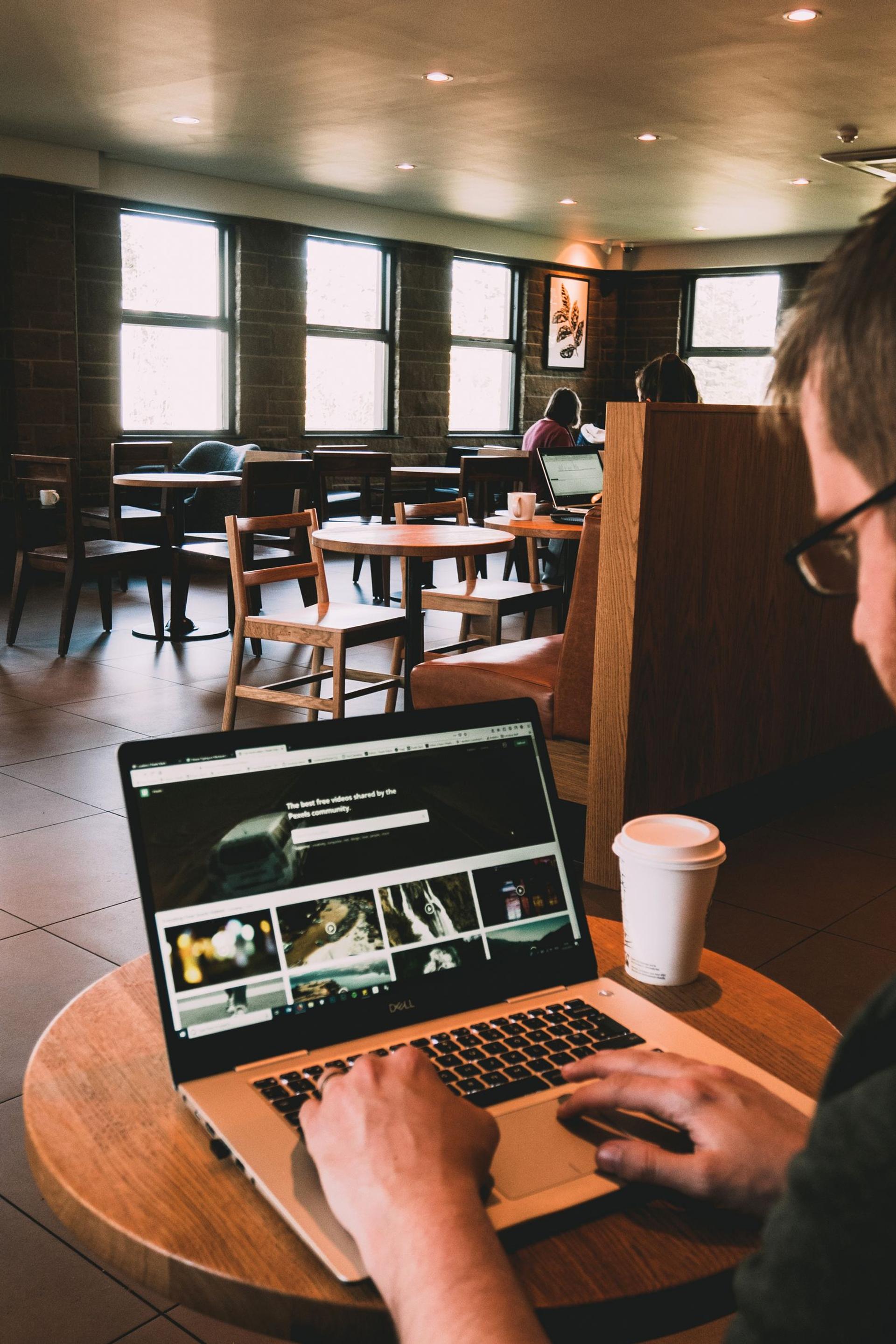 Person browsing a laptop at a table in a cafe