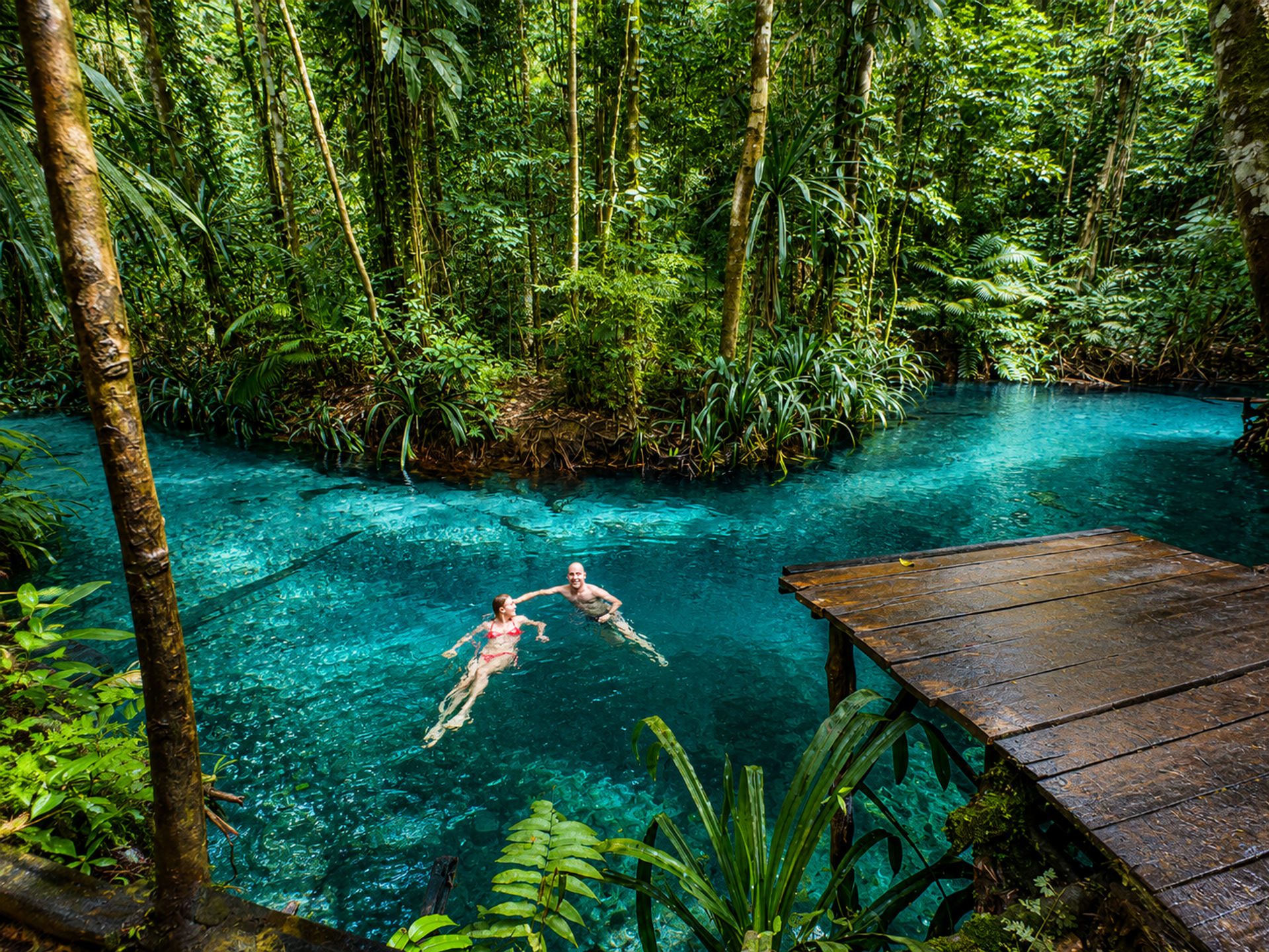 Two guests floating in the  blue river enclosed by dense jungle