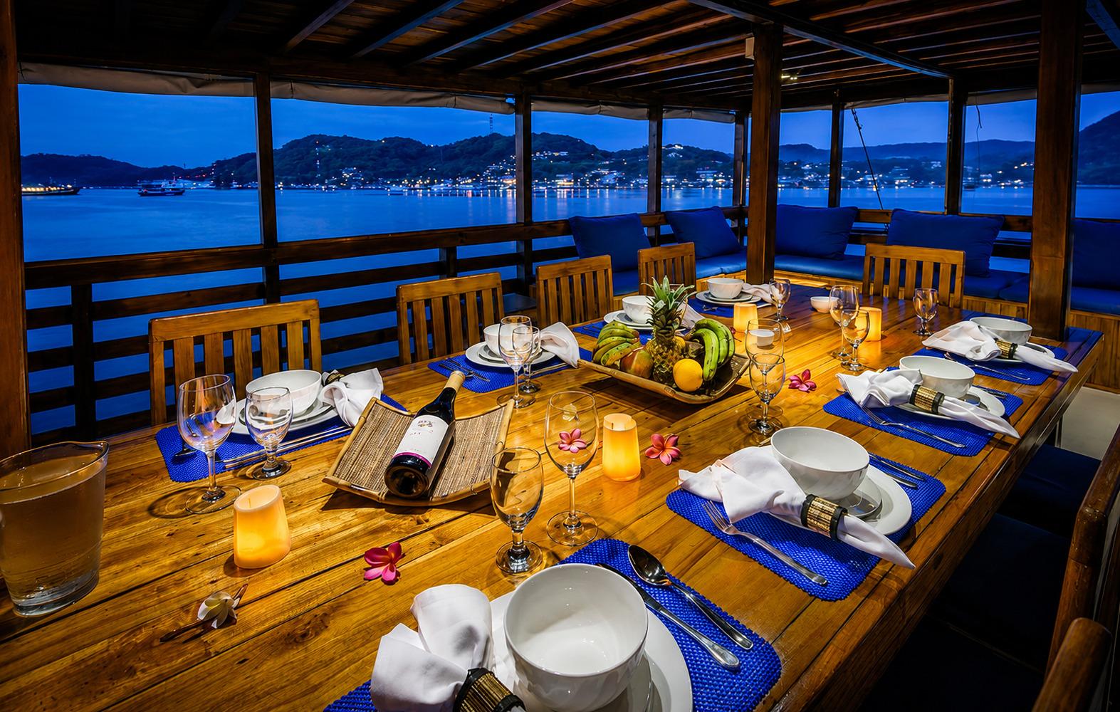 Al fresco dining deck of Mari Liveaboard set for dinner at dusk, with candles and sea views