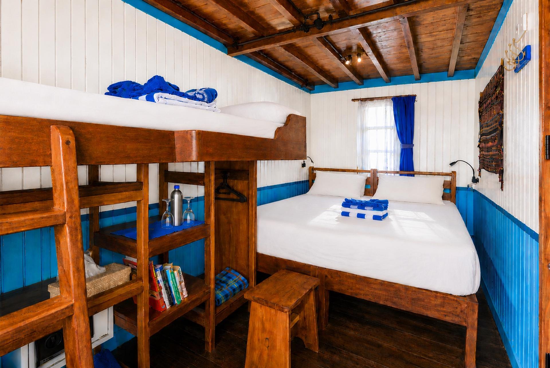 Deluxe cabin on Mari with a double bed made up in white linen, teak floor and turquoise panelled walls