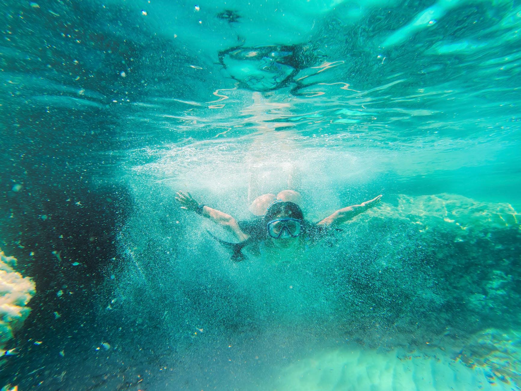 Snorkeler diving down through bubbles in clear turquoise water