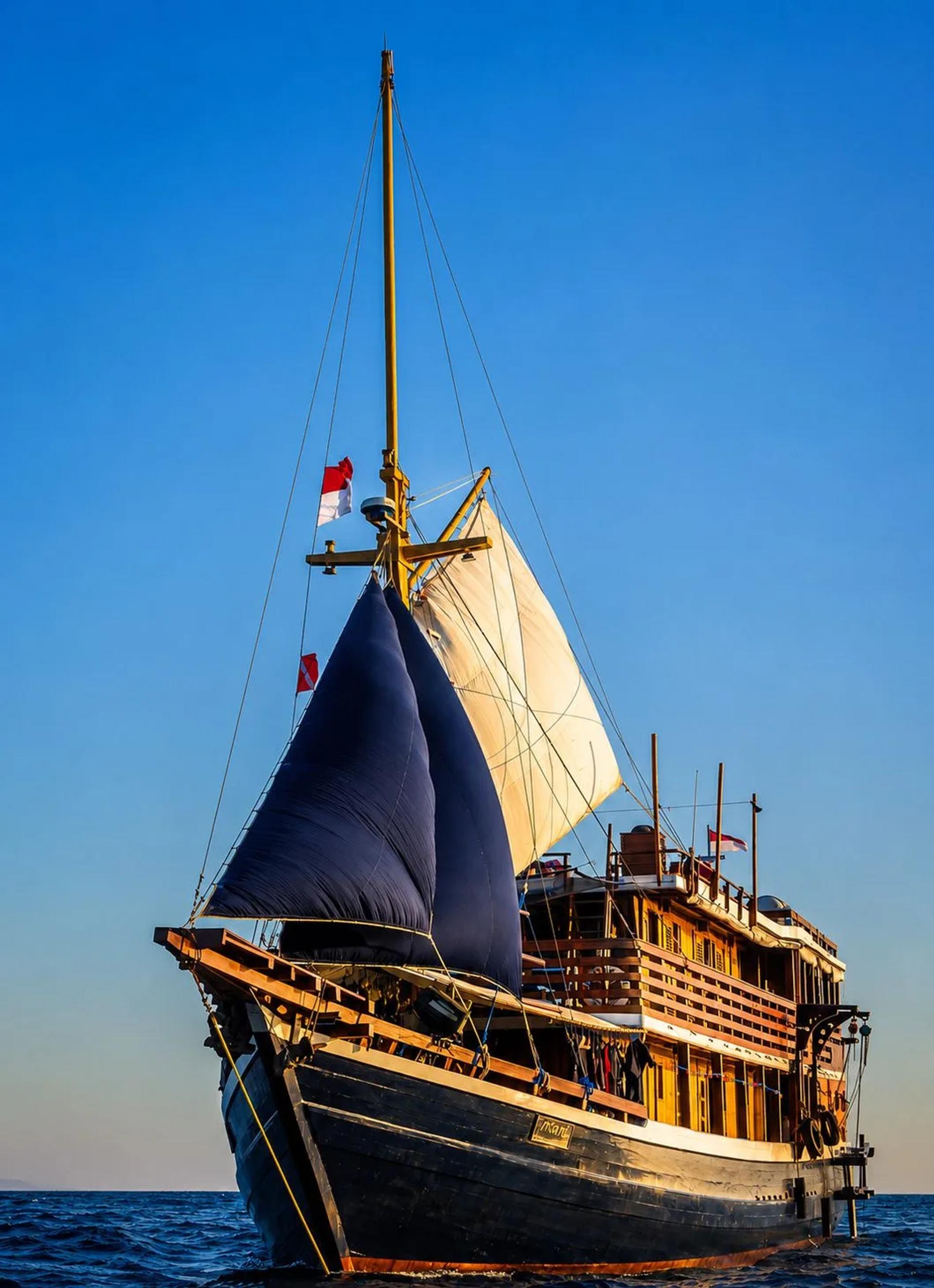 The Mari phinisi under sail against a clear blue sky