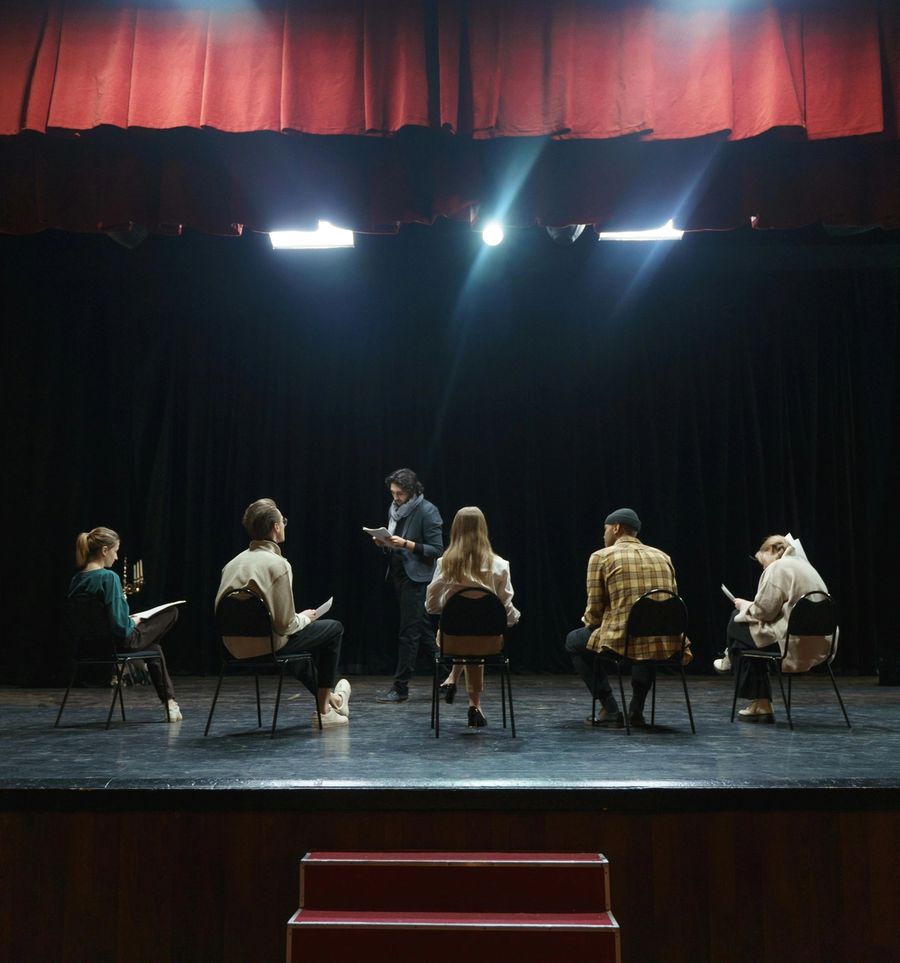 5 attori seduti sul palco di un teatro