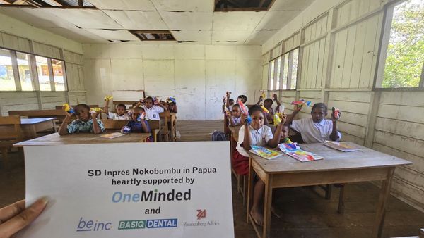 Een klas vol kinderen die hun nieuwe tandenborstel omhooghouden, met op de voorgrond een bord met SD Inpres Nokobumbu en de partners Be-inc, Basiq Dental en Zwanenberg Advies.