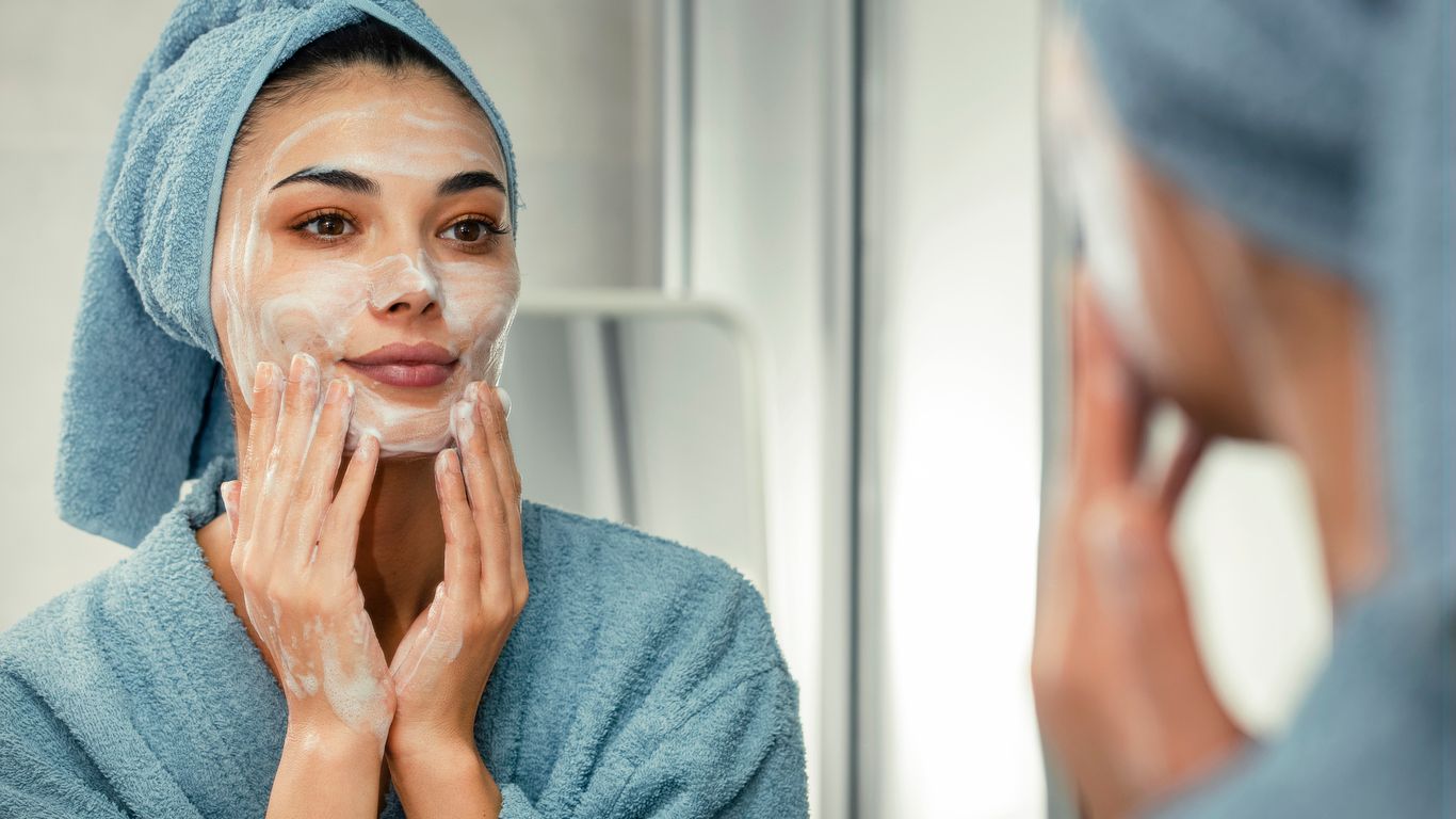 A young woman applying facial cleanser after exiting the shower in a robe