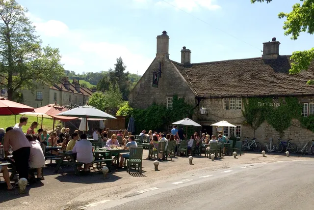 The George Inn in Bathampton: Front view with people enjoying outdoor seating on a sunny day, embracing the delightful ambiance of this picturesque pub