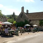 The George Inn in Bathampton: Front view with people enjoying outdoor seating on a sunny day, embracing the delightful ambiance of this picturesque pub