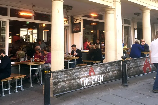 The Oven in Bath: Front view with patrons enjoying outdoor dining, savouring delicious food in a vibrant atmosphere at this popular restaurant