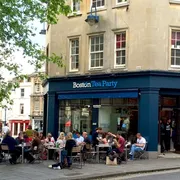 Boston Tea Party in Bath: Bustling front view with people enjoying outdoor seating, savouring delicious treats amidst a lively atmosphere