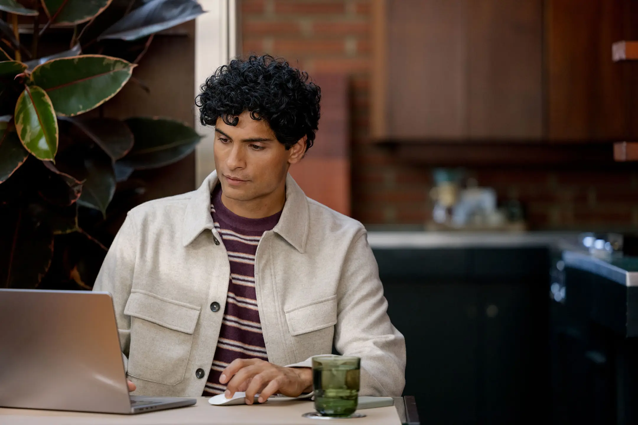A man with curly hair uses a laptop and mouse at a table.