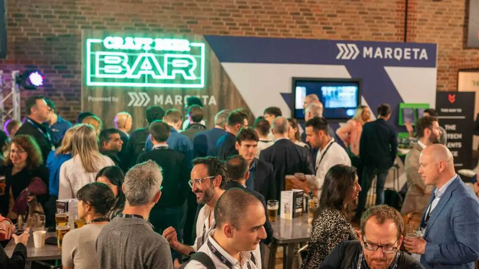 People socializing at an event with a 'Craft Beer Bar' sponsored by Marqeta.