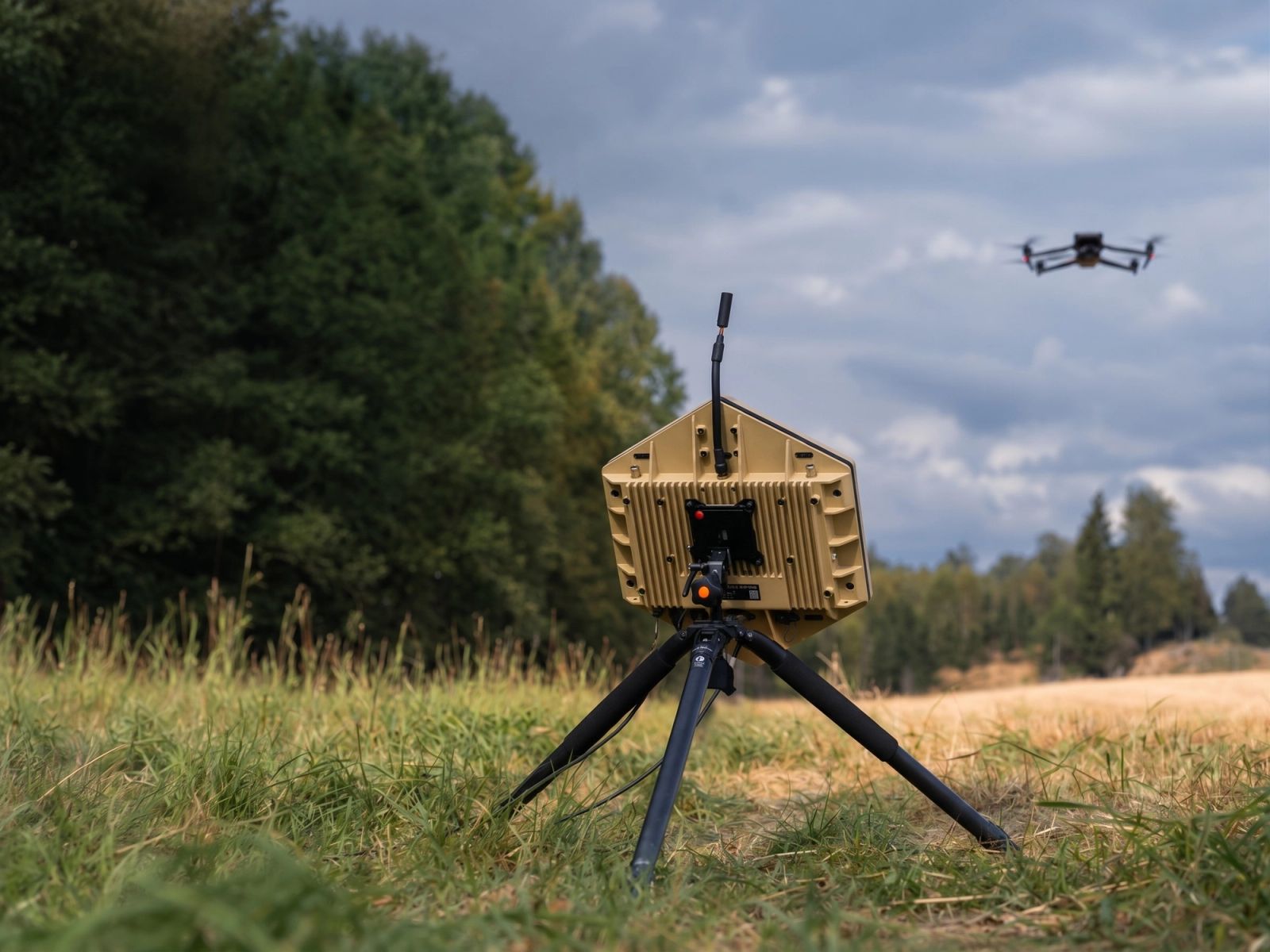 Acoustic sensor on a tripod in a field, with a drone in the sky