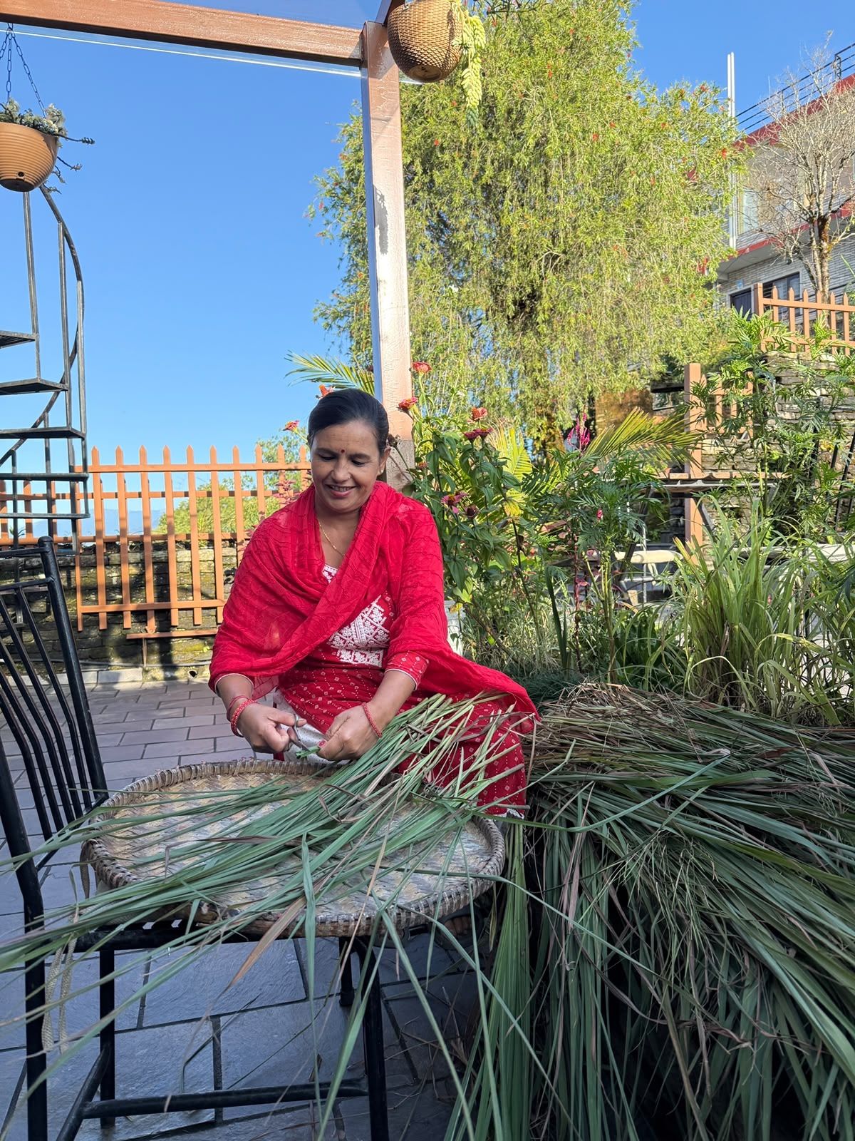 Maya cutting lemongrass onto a round woven tray in the garden