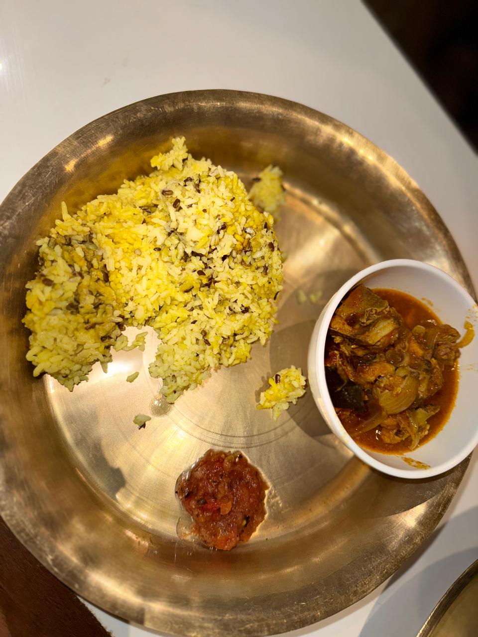 A brass plate of rice with curry and achar