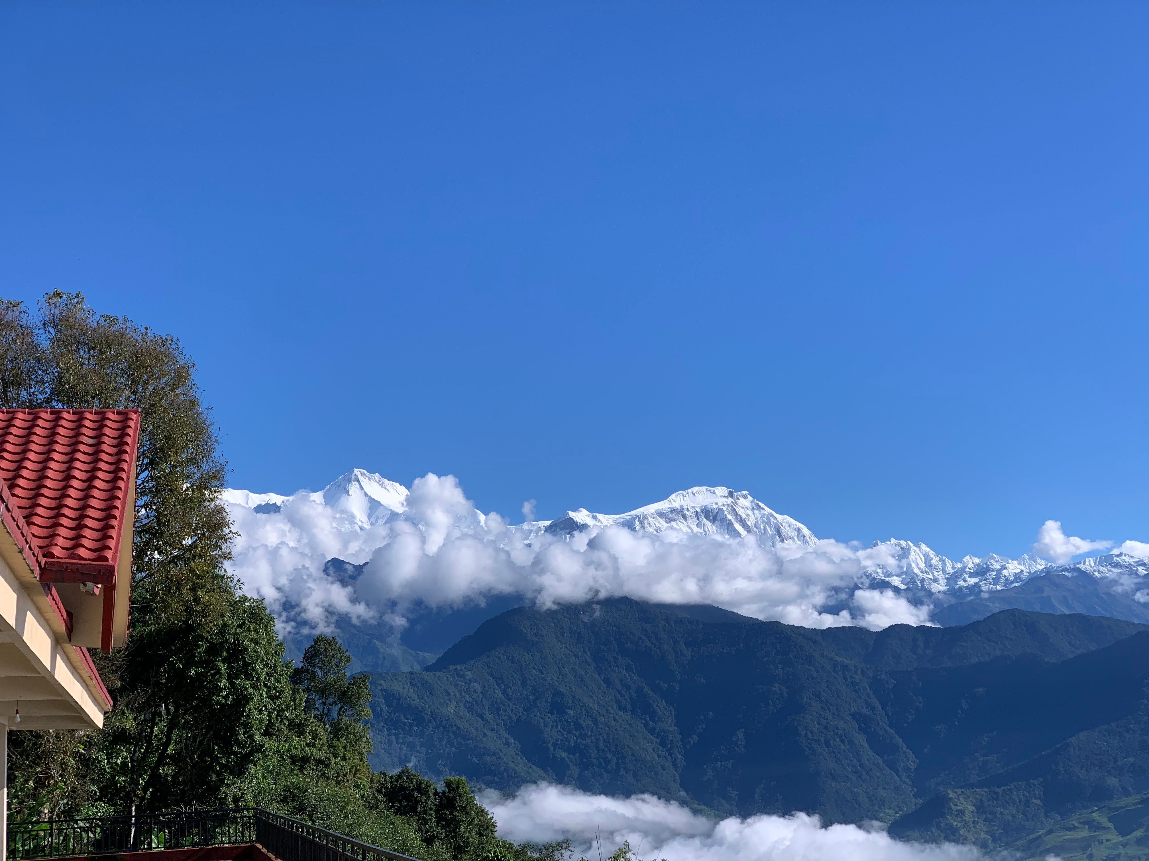 Snow mountains above clouds on a clear morning, red roof in the foreground