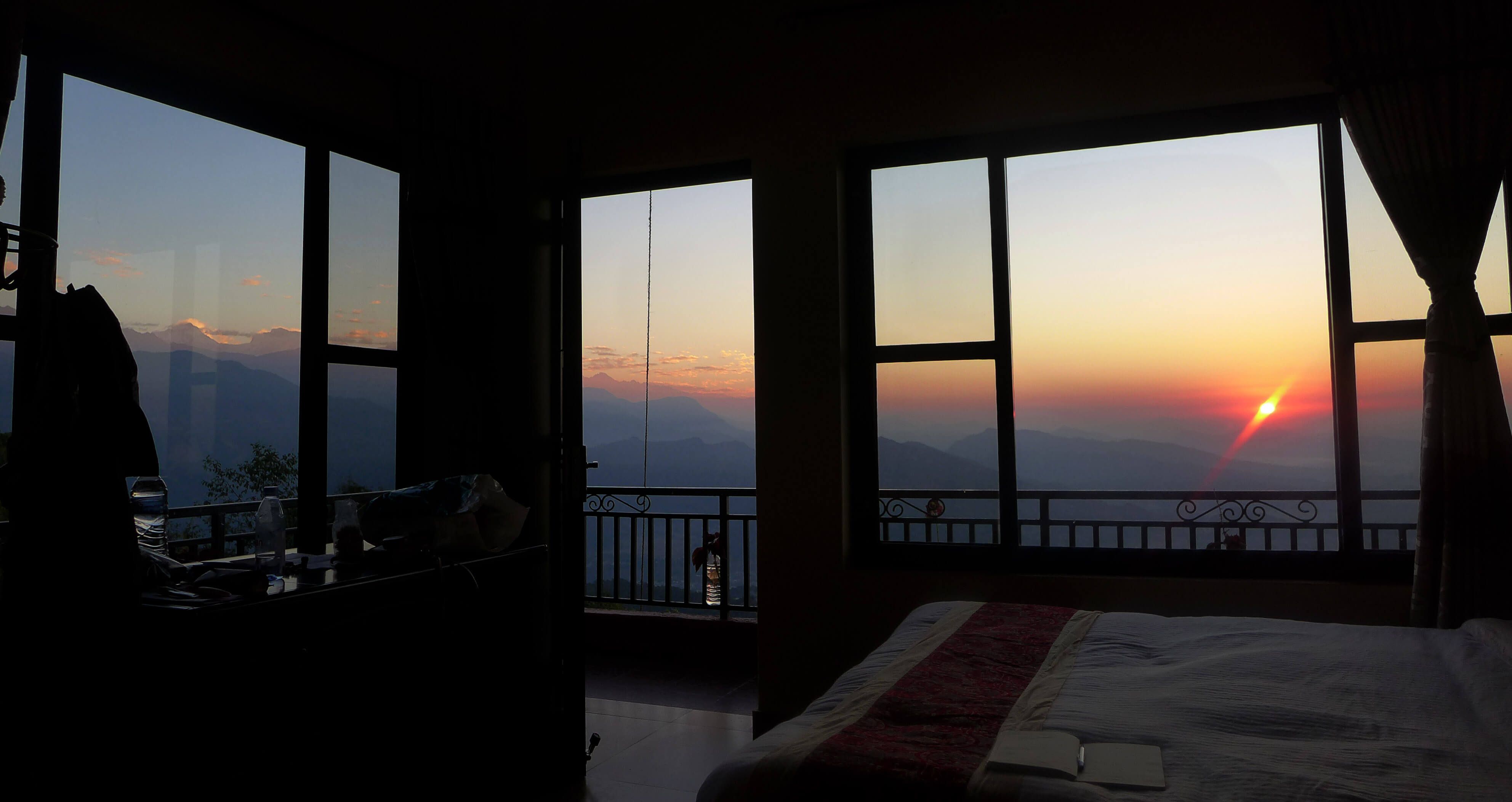 A guest room at dawn, the sun rising over the hills through tall windows