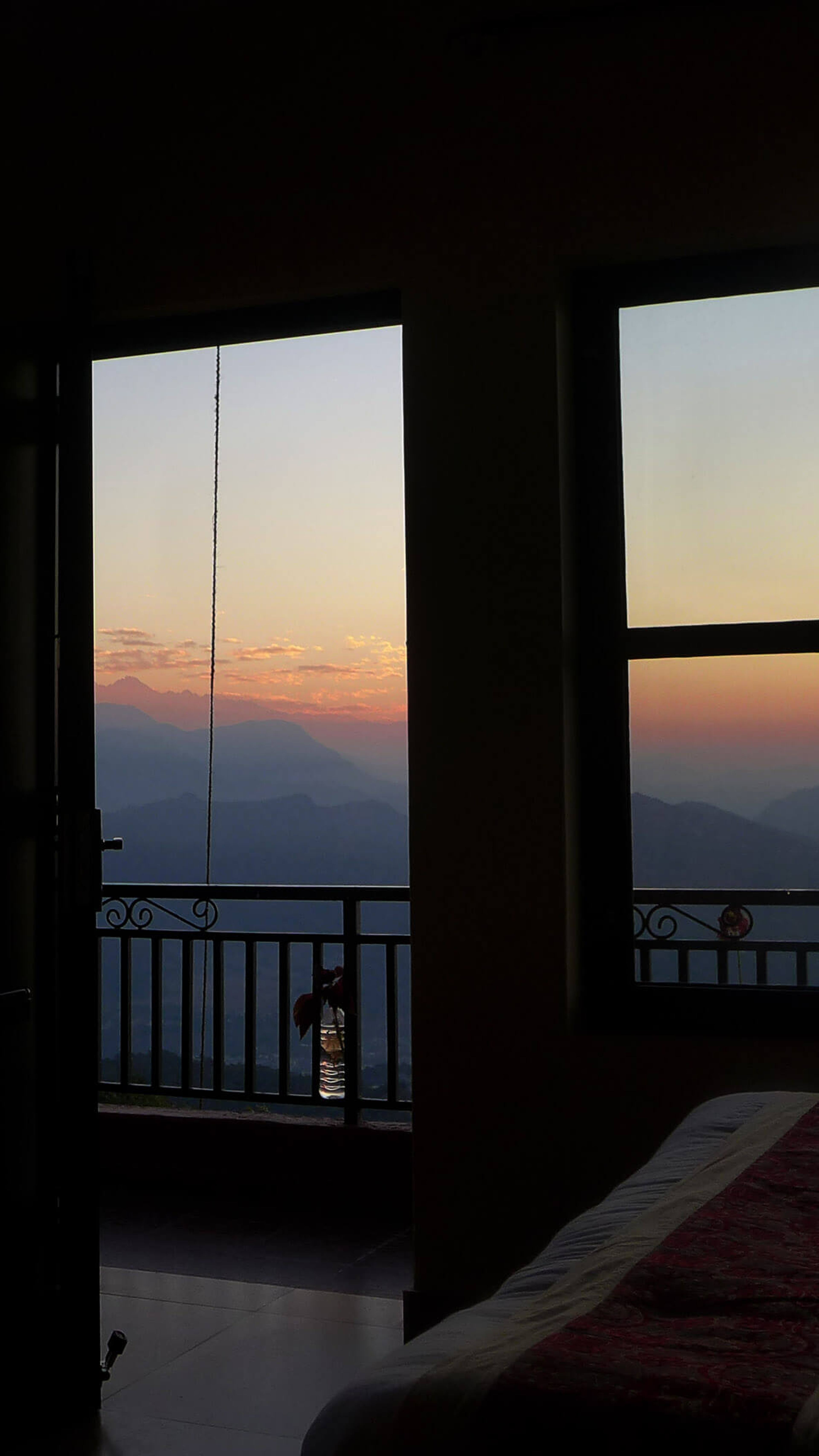 A guest room at dawn, the sun rising over the hills through tall windows