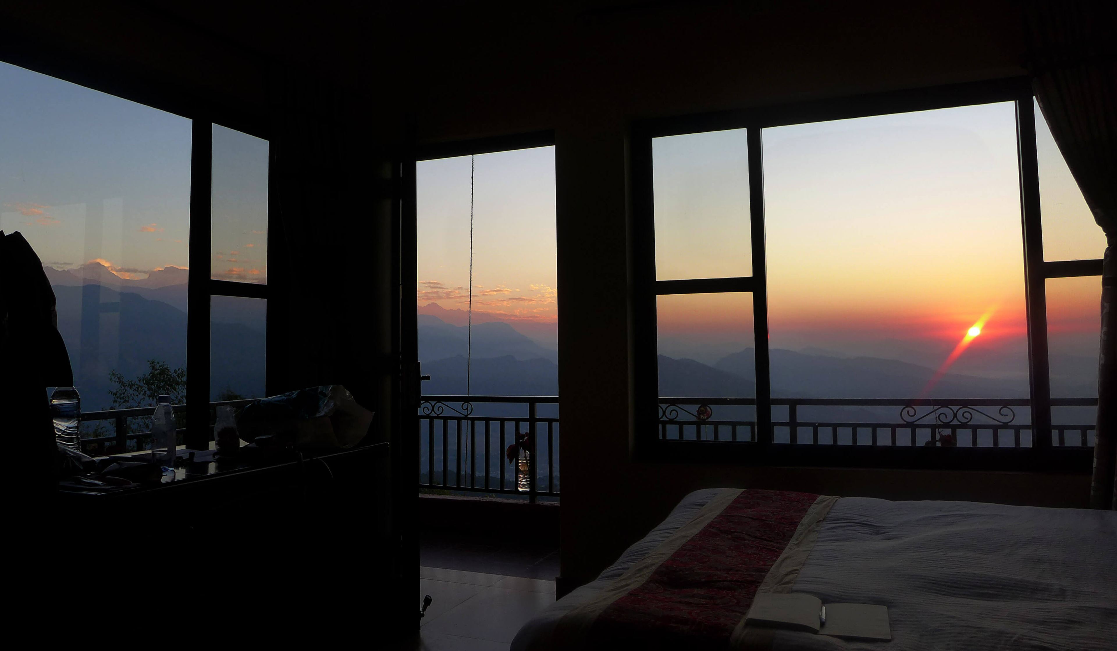 A guest room at dawn, the sun rising over the hills through tall windows
