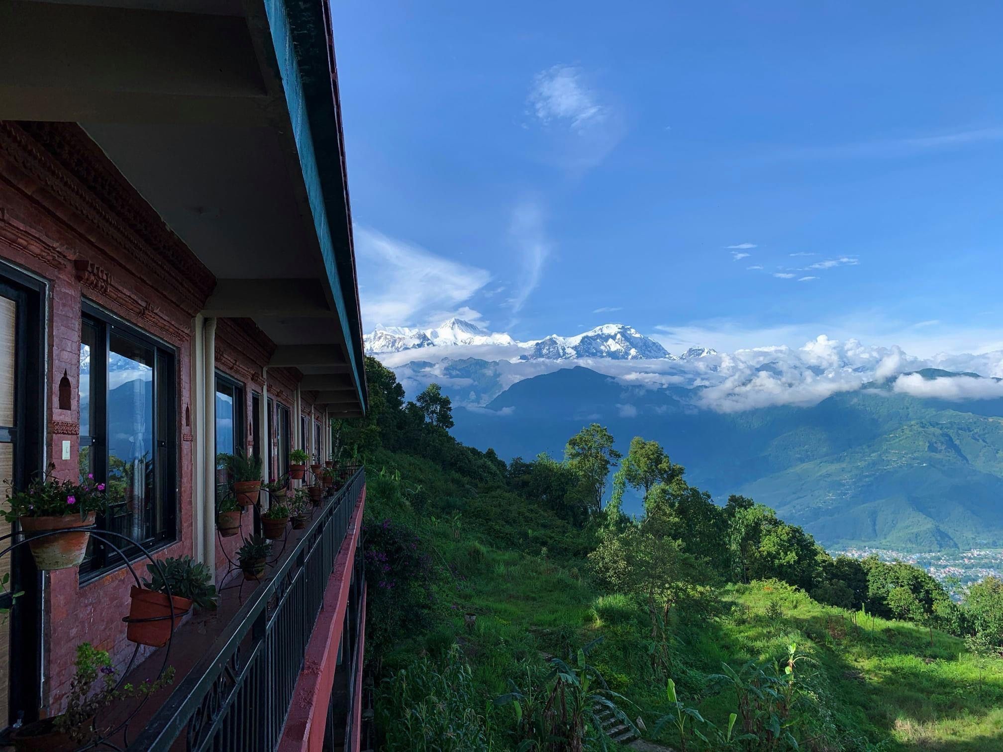 The lodge's balcony with flower pots, overlooking green hills and the snow-covered Annapurna range
