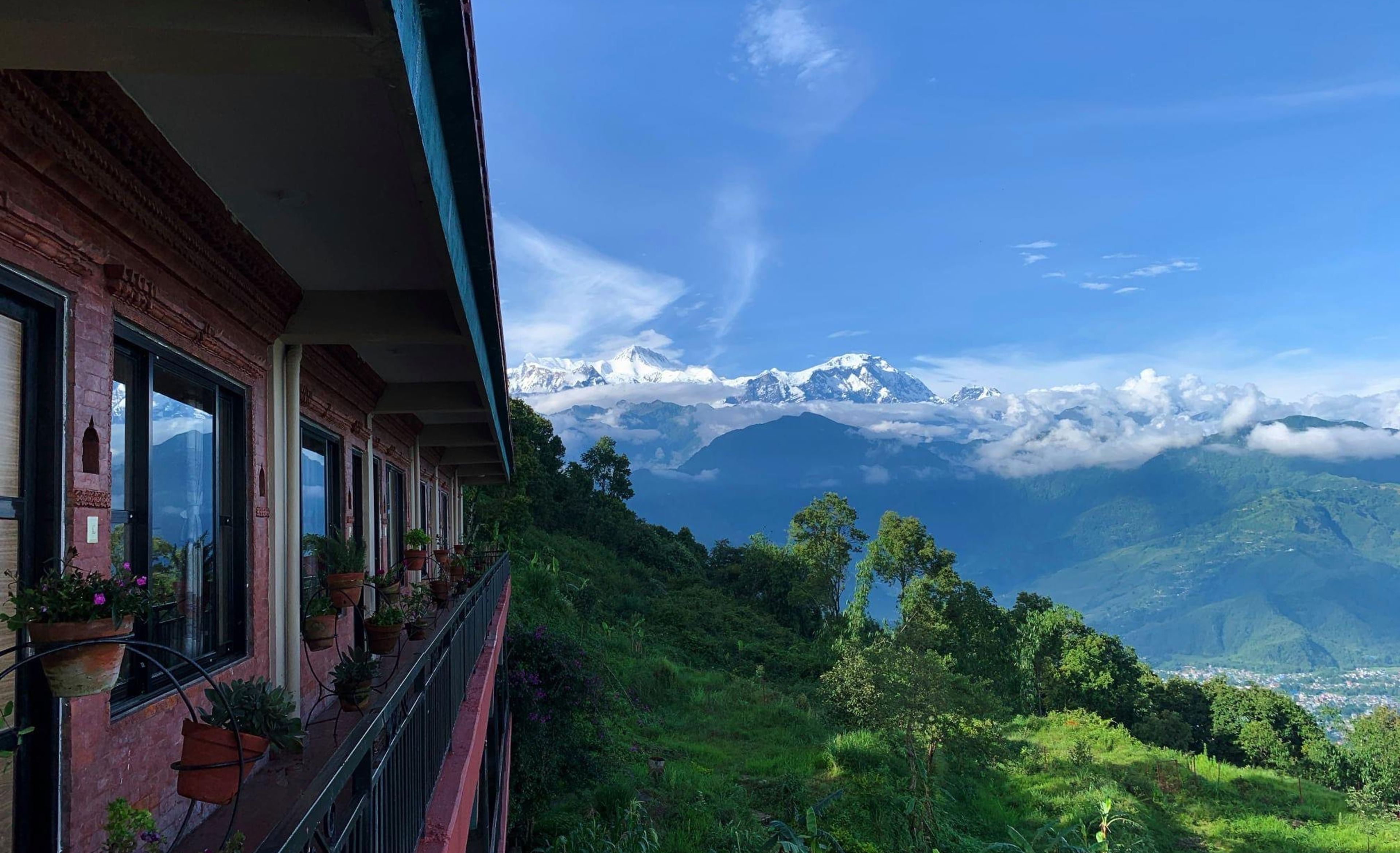 The lodge's balcony with flower pots, overlooking green hills and the snow-covered Annapurna range