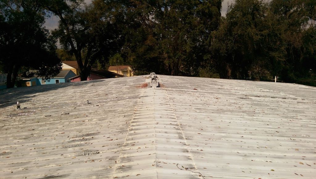 Ridge line of the old painted metal roof, with rust staining and leaf debris built up in the panel grooves.