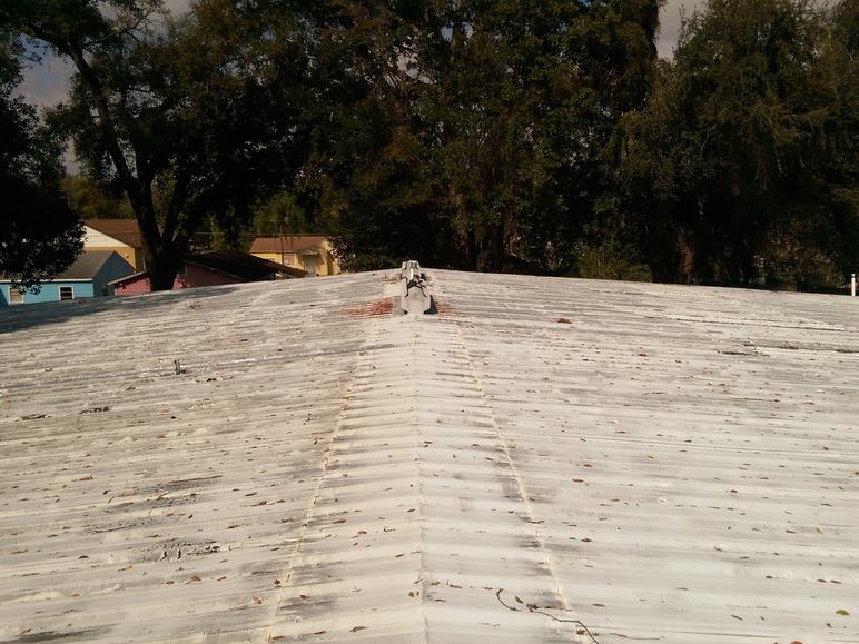 Ridge line of the old painted metal roof, with rust staining and leaf debris built up in the panel grooves.