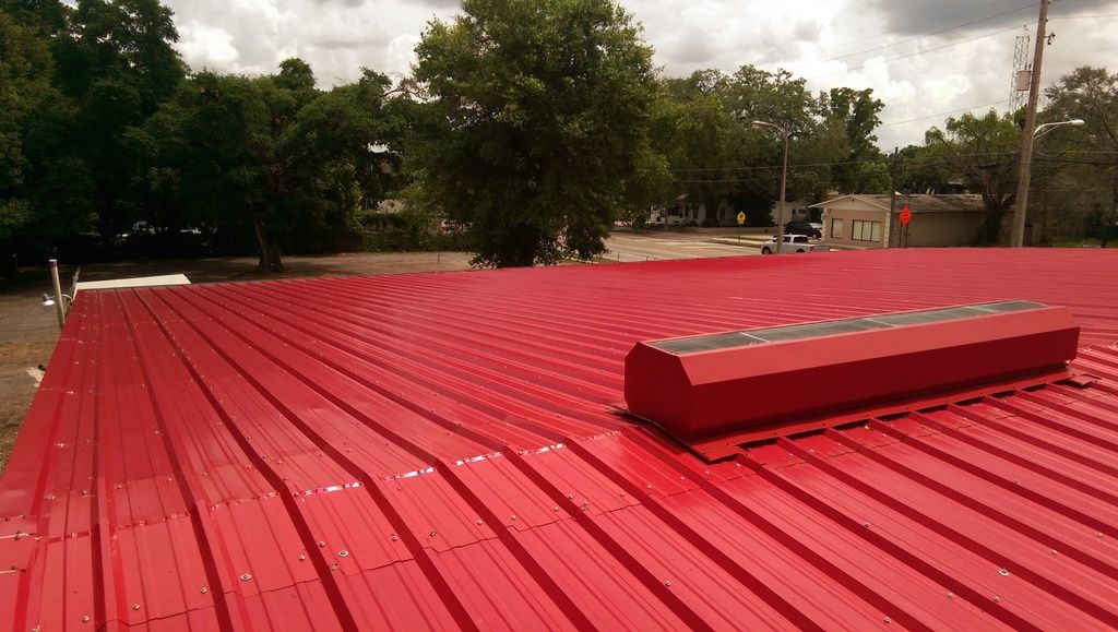 New red metal roof panels installed cleanly along the ridge, replacing the old rusted panels.