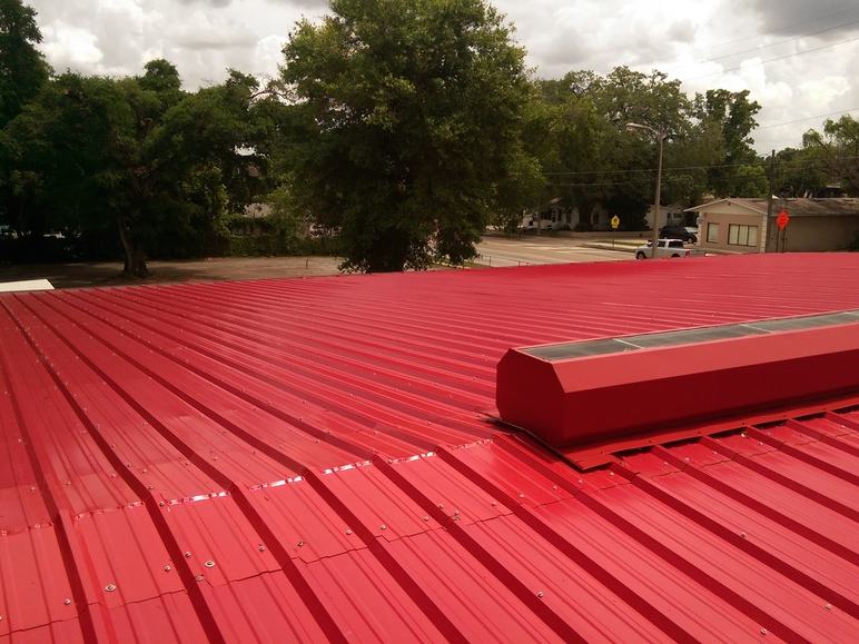 New red metal roof panels installed cleanly along the ridge, replacing the old rusted panels.
