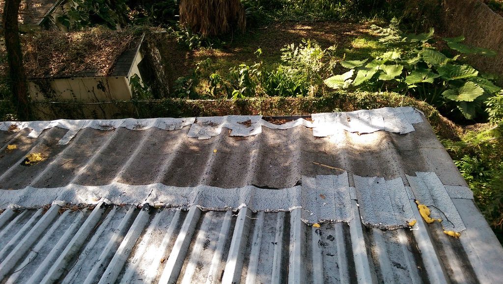 Close-up of the old roof panels, showing torn, curling material along the seams.