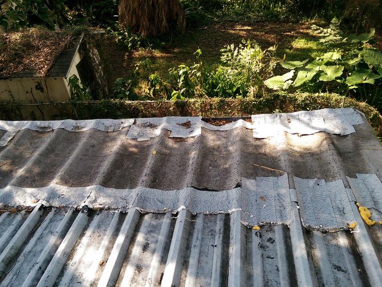 Close-up of the old roof panels, showing torn, curling material along the seams.