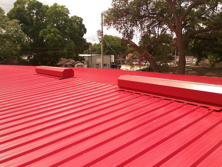 New red standing-seam metal roof with two new ridge vents installed for attic airflow.