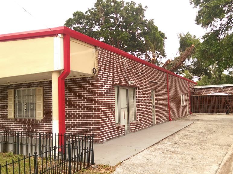 Wide view of the building after the re-roof, with a new red roofline edge and matching red gutter trim.
