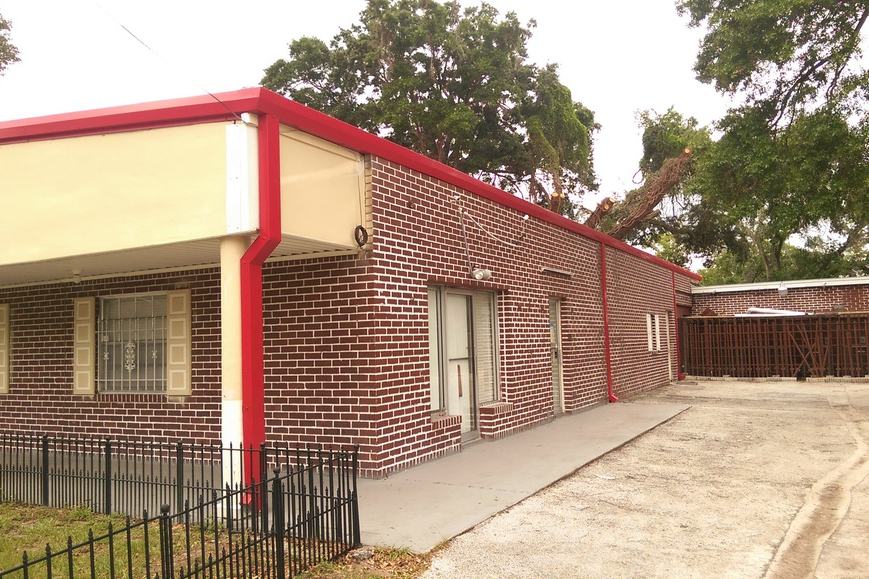 Wide view of the building after the re-roof, with a new red roofline edge and matching red gutter trim.