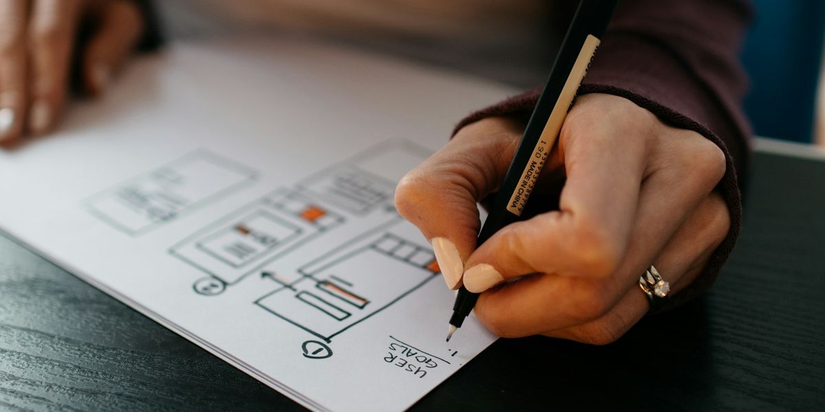Tangan menggambar sketsa tata letak halaman di atas kertas, tahap perencanaan cara bikin website company profile
