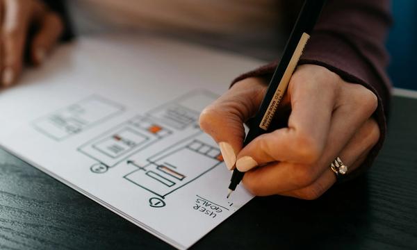 Tangan menggambar sketsa tata letak halaman di atas kertas, tahap perencanaan cara bikin website company profile