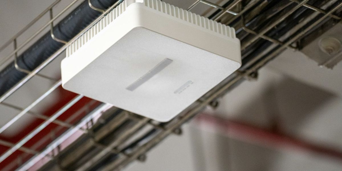 Access point Wi-Fi putih terpasang di kabel tray plafon kantor, perangkat yang menentukan apakah Wi-Fi kantor lambat saat jam sibuk