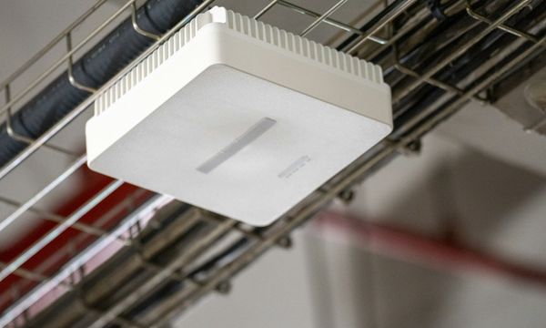 Access point Wi-Fi putih terpasang di kabel tray plafon kantor, perangkat yang menentukan apakah Wi-Fi kantor lambat saat jam sibuk