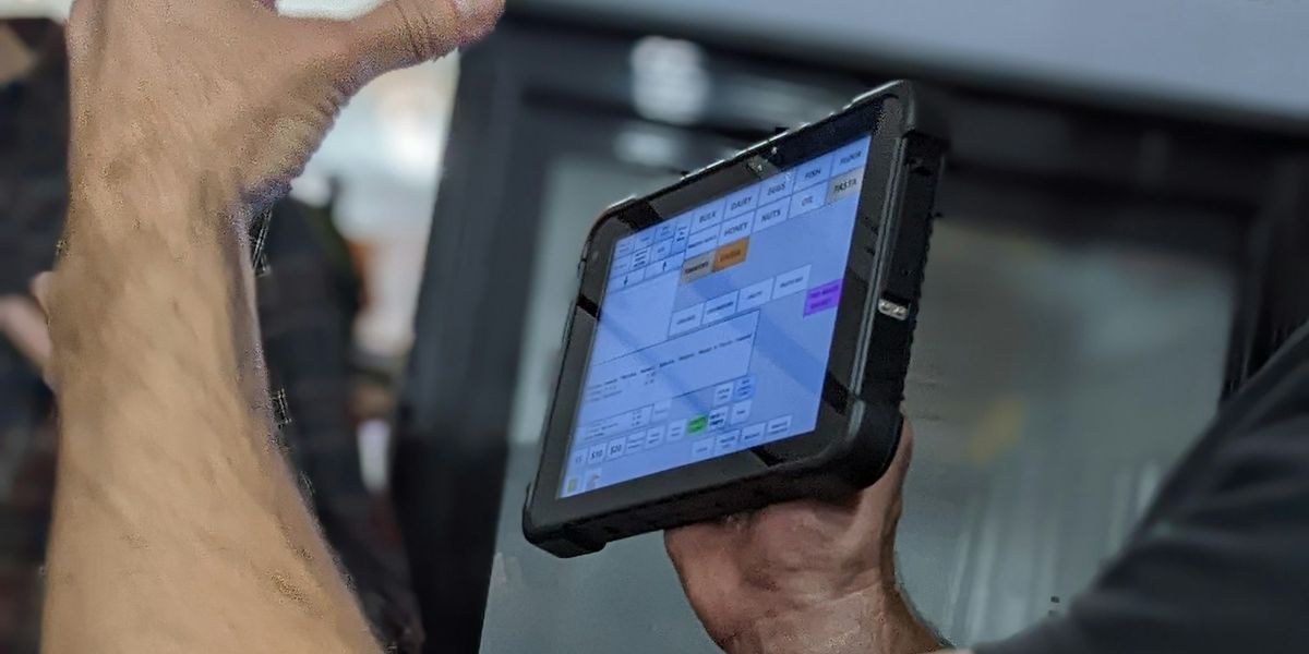 Shop staff holding a tablet running point-of-sale software with a grid of grocery product categories on screen