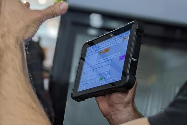 Shop staff holding a tablet running point-of-sale software with a grid of grocery product categories on screen