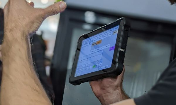 Shop staff holding a tablet running point-of-sale software with a grid of grocery product categories on screen