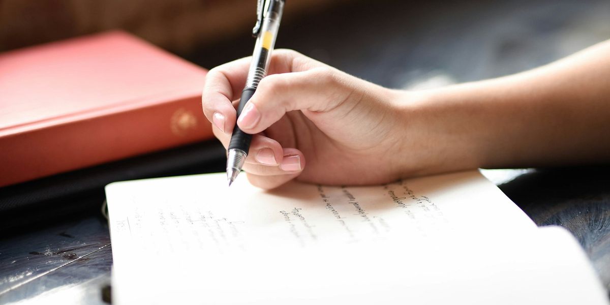 Tangan menulis dengan pulpen di atas lembar kertas, tanda tangan basah yang digantikan tanda tangan digital pada berkas PDF