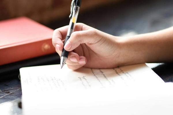 Tangan menulis dengan pulpen di atas lembar kertas, tanda tangan basah yang digantikan tanda tangan digital pada berkas PDF
