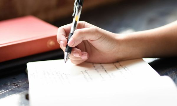 Tangan menulis dengan pulpen di atas lembar kertas, tanda tangan basah yang digantikan tanda tangan digital pada berkas PDF